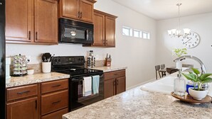 A modern kitchen with wooden cabinets, a black microwave, a stove, and a sink with a plant. - ❃Close to the POOL! 3BD/2BA! Close to BSU/Nampa/Kuna! Your Boise Vacation Spot!❃ (Meridian)