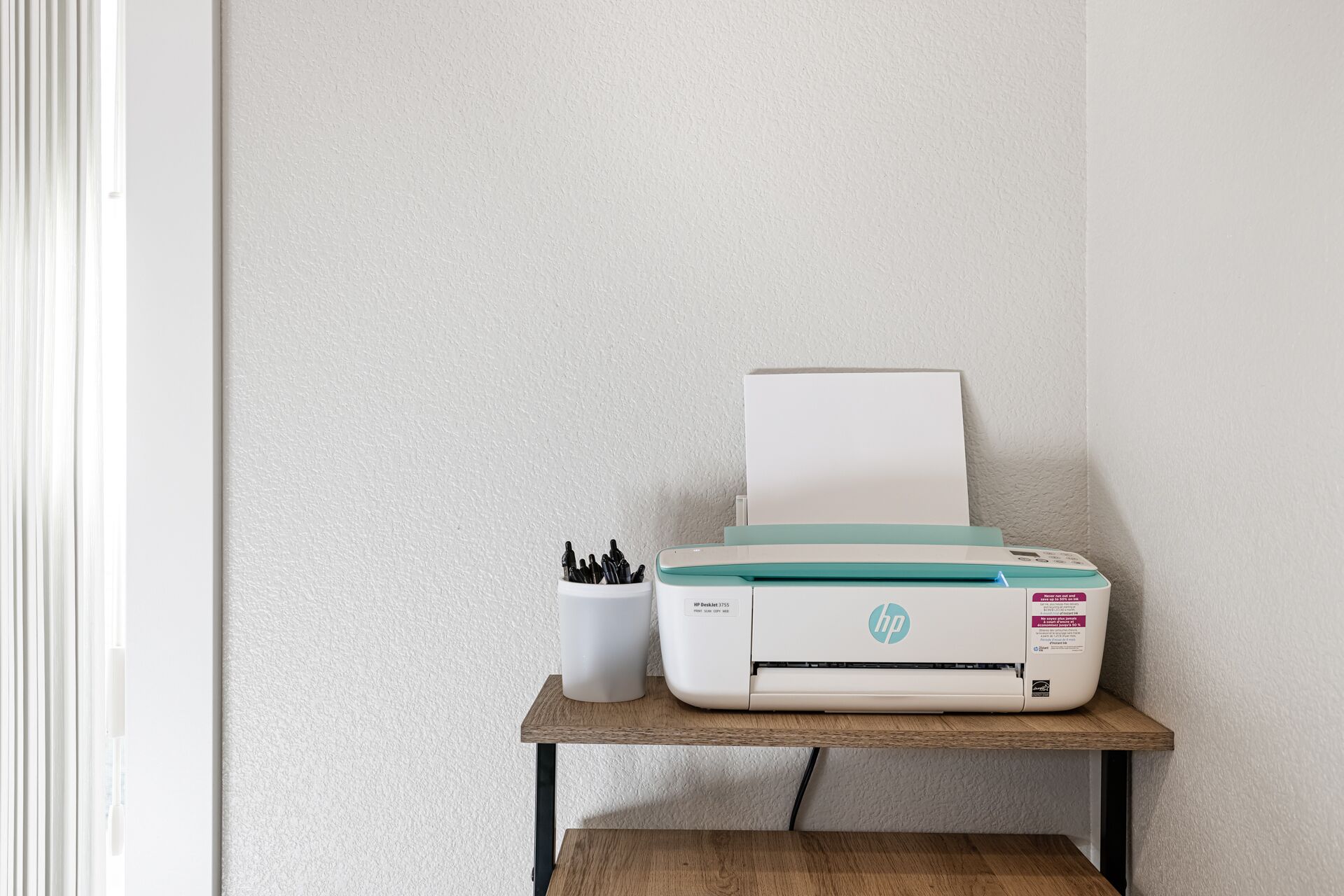 A printer on a wooden shelf against a textured wall.