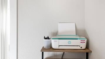 A printer on a wooden shelf against a textured wall.