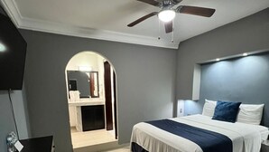 Un dormitorio con una cama, ventilador de techo, televisor y escritorio.