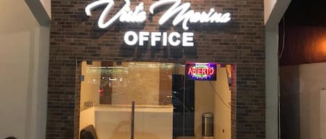 The exterior of Viva Marina Office with a neon sign, a glass entrance, and a visible trash can outside.