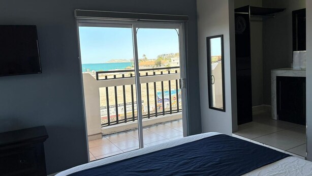 Un dormitorio con cama, televisor, balcón con vista al mar y chimenea.