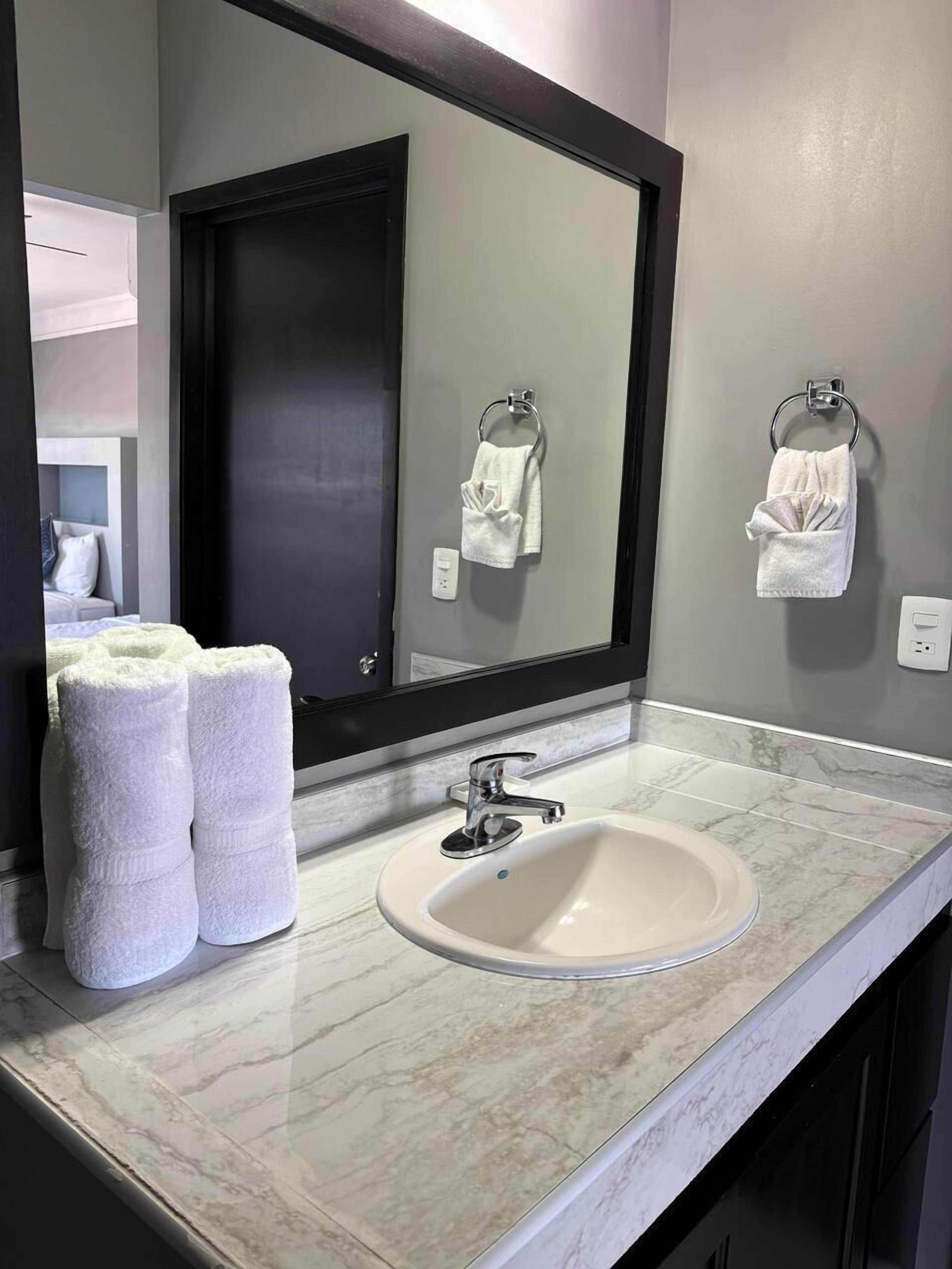A bathroom with a white sink, a large mirror, and two towels on the wall.