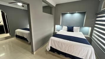 Un dormitorio moderno con una cama grande, una cama más pequeña, un ventilador de techo y una ventana con persianas.