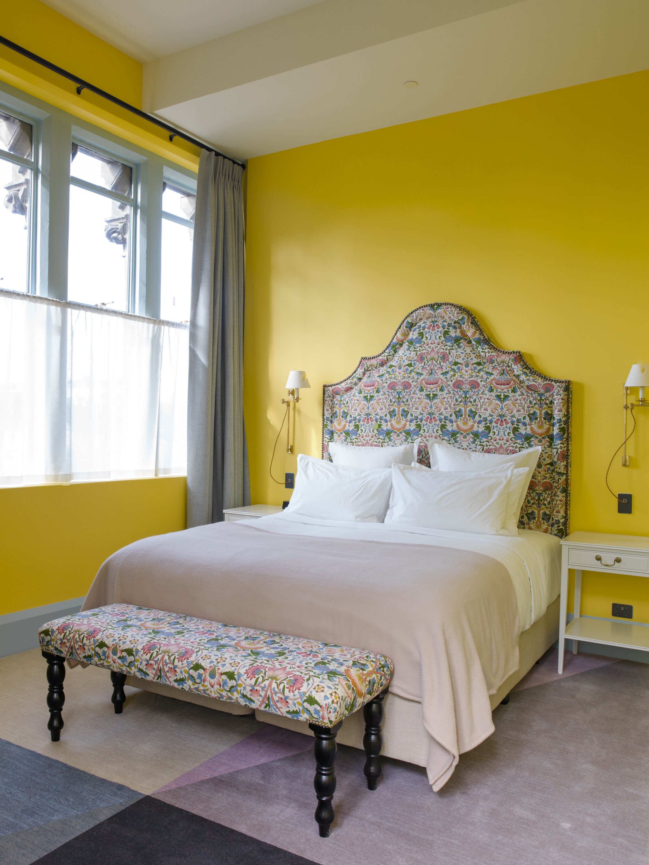 A bedroom with a bed, bedside tables, a bench, and a window with curtains.
