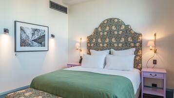 A neatly arranged bedroom with a large bed, a bedside table, a nightstand, a bench, and a wall-mounted picture.