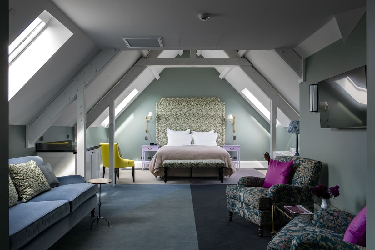 Ein Schlafzimmer mit Schrägen, einem Bett, einer Couch, zwei Sesseln und einem kleinen Tisch.