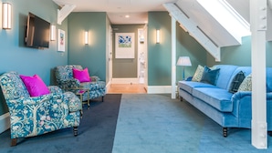 Un salon aux murs de couleur turquoise, avec un canapé bleu, des fauteuils à motifs et un téléviseur à écran plat.
