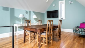 Une salle à manger avec une table et des chaises en bois, une lampe blanche, un téléviseur accroché au mur et une fenêtre.