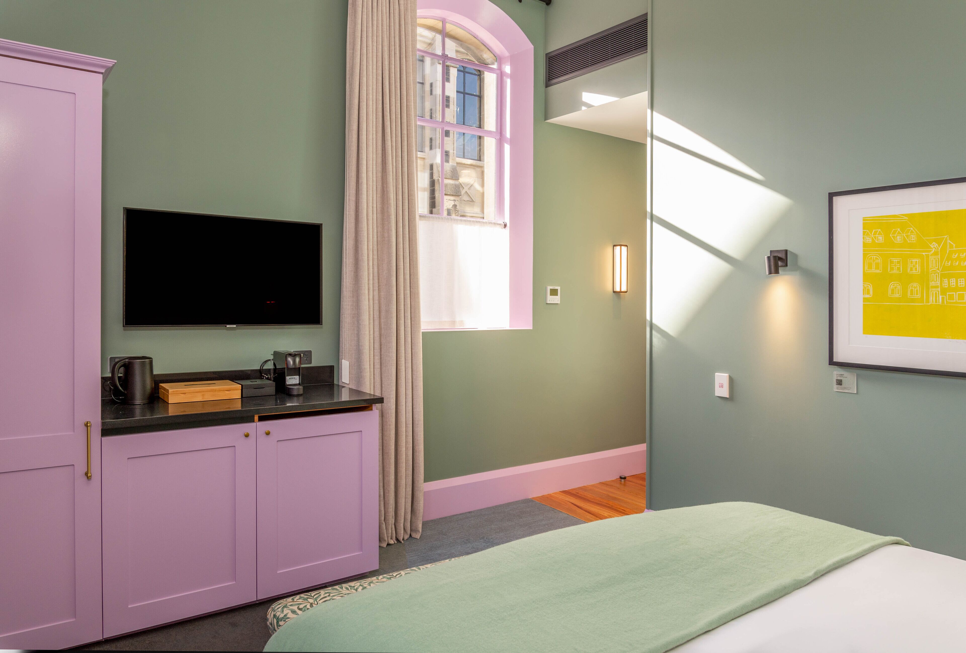 A bedroom with a bed, a television, a wardrobe, a window with curtains, and a framed picture on the wall.