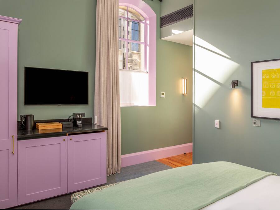 A bedroom with a bed, a television, a wardrobe, a window with curtains, and a framed picture on the wall.