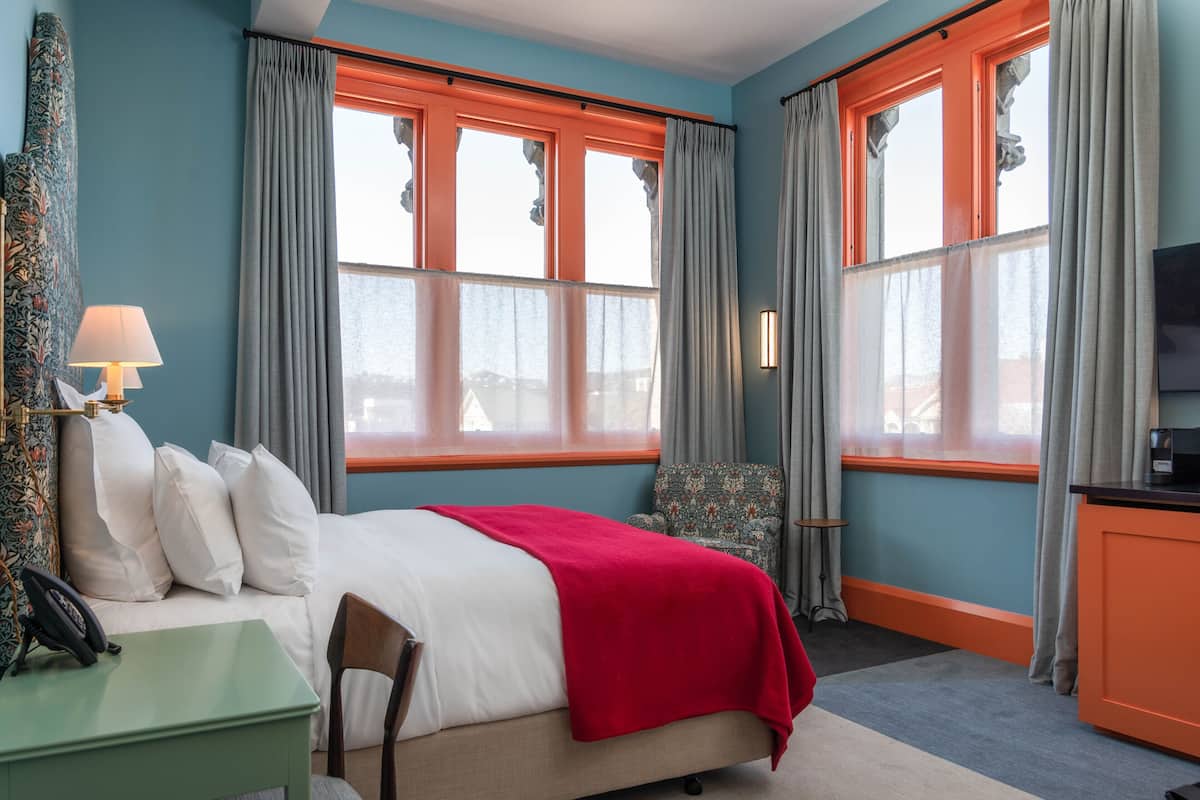 Ein Hotelzimmer mit Bett, Schreibtisch, Stuhl, Schreibtischlampe und Fernseher.