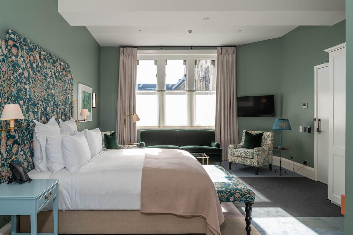 Ein Hotelzimmer mit einem großen Bett, einem Schlafsofa, einem Sessel, einem Fernseher und einem Fenster mit Vorhängen.
