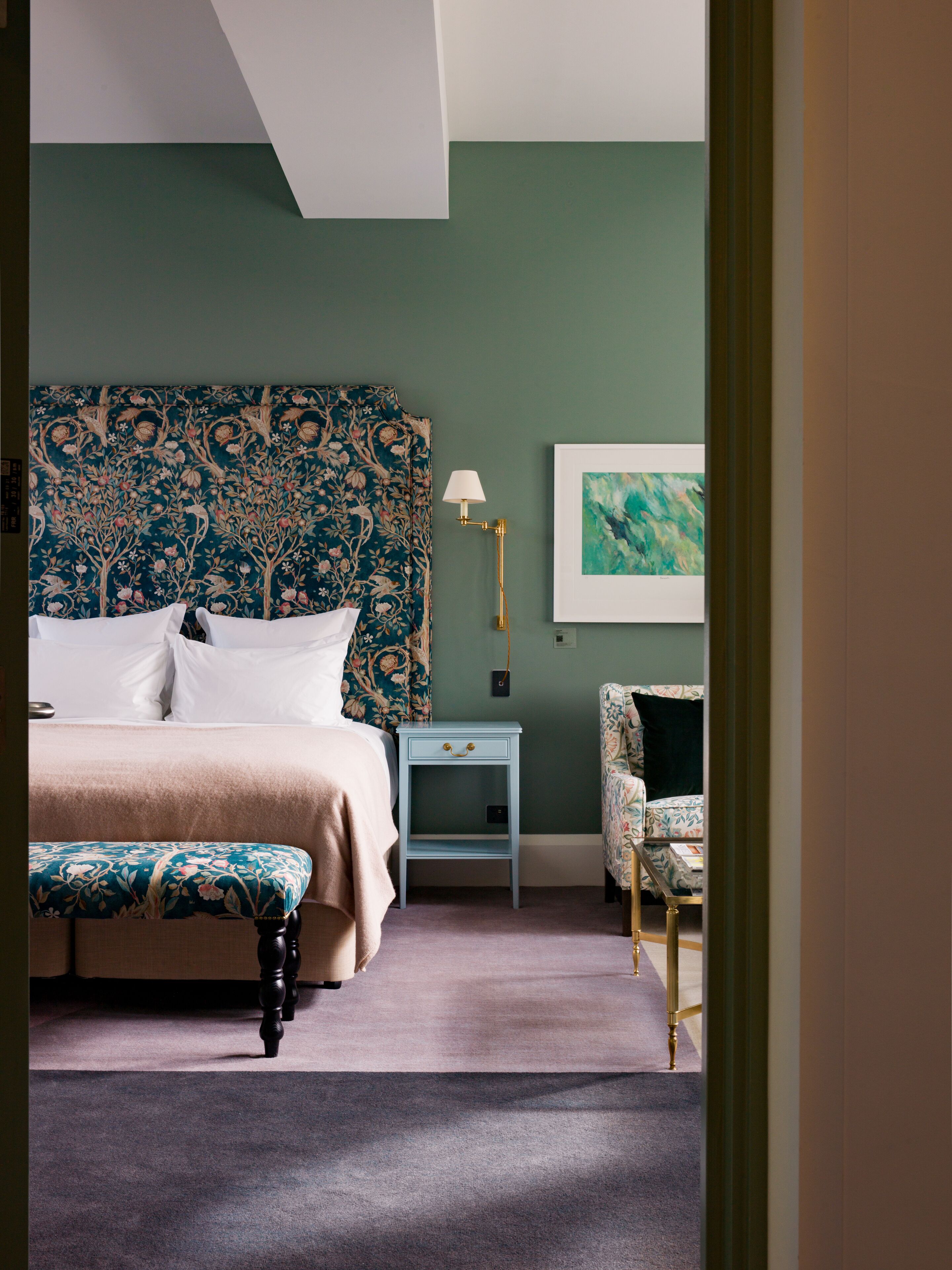 A bedroom with a bed, a nightstand, a chair, a lamp, and a framed picture on the wall.
