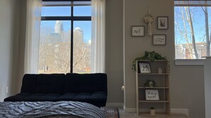 Un dormitorio con un ventanal grande, una cama, una estantería y una planta pequeña.