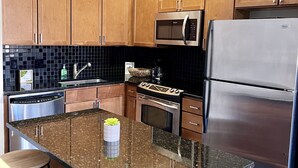 Una cocina moderna con armarios de madera, refrigerador de acero inoxidable, microondas y encimera de granito.