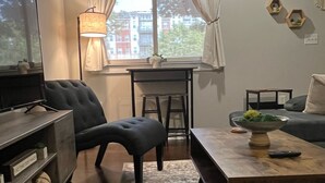 Una sala de estar con sofá, reposapiés, televisor, mesa de centro y ventana con cortinas.