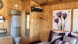 A wooden cabin-style bedroom with a bed, a wooden ceiling, and a bathroom visible through an open door. - Tiny Cottages in Cloudcroft/ Mayhill  NM (Mayhill)