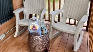 A wooden deck with two chairs and a table, a bottle of wine, and a glass pitcher with grapes. - Tiny Cottages in Cloudcroft/ Mayhill  NM (Mayhill)