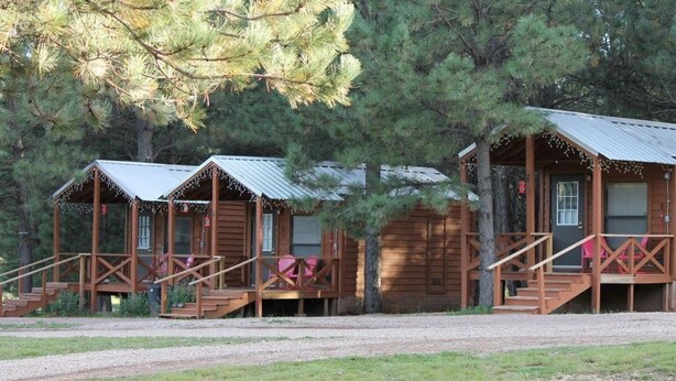 A row of wooden cabins with metal roofs, each featuring a porch and stairs leading to the entrance. - Tiny Cottages in Cloudcroft/ Mayhill  NM (Mayhill)