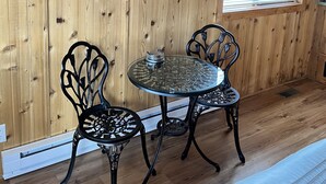 A room with wooden walls, a round glass table with chairs, a window with blinds, and a radiator. - Tiny Cottages in Cloudcroft/ Mayhill  NM (Mayhill)