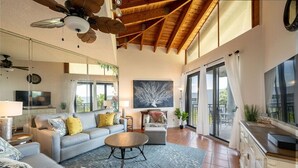 Un salón amplio con techos altos, un cuadro grande y vistas a través de puertas de cristal.