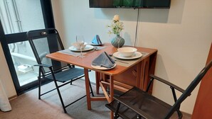 Un coin repas avec une table dressée pour deux personnes, un vase rempli de fleurs et un téléviseur fixé au mur.