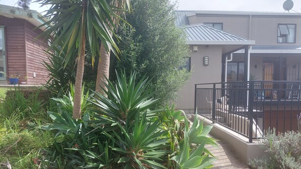 Un quartier résidentiel avec une maison dotée d’un balcon orné d’une rambarde noire, le tout entouré de diverses plantes et arbres.