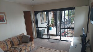 Un salon comprenant un canapé, un tapis, un téléviseur et une porte-fenêtre coulissante donnant sur un espace extérieur avec un balcon.