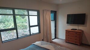 Une chambre à coucher avec un lit, une commode, un téléviseur et une fenêtre avec des rideaux.