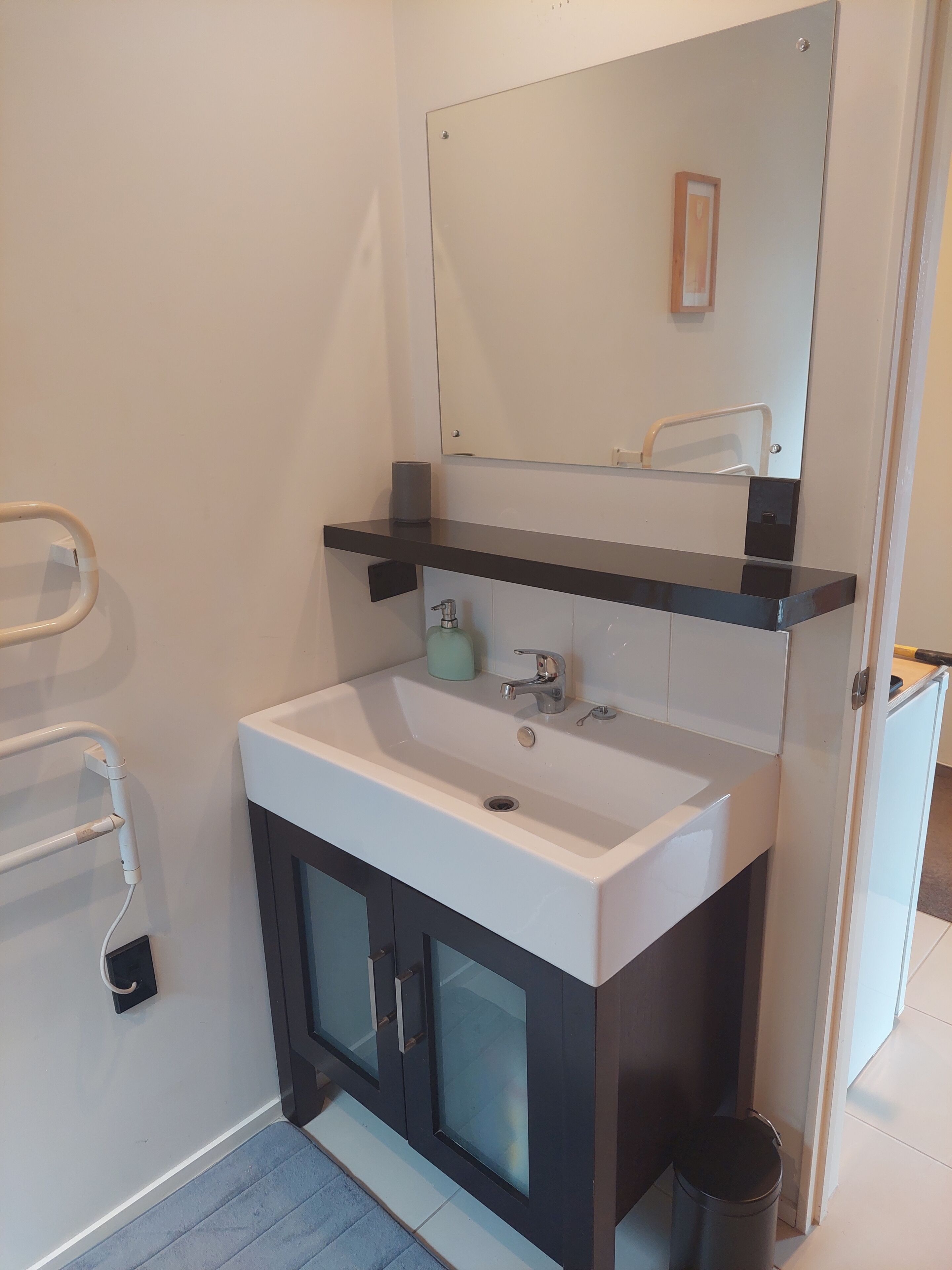 Ein Badezimmer mit weißem Waschbecken, einem Spiegel und einem Handtuchhalter.