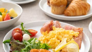 A breakfast setting with plates of food, including eggs, ham, and shrimp, and a cup of coffee.