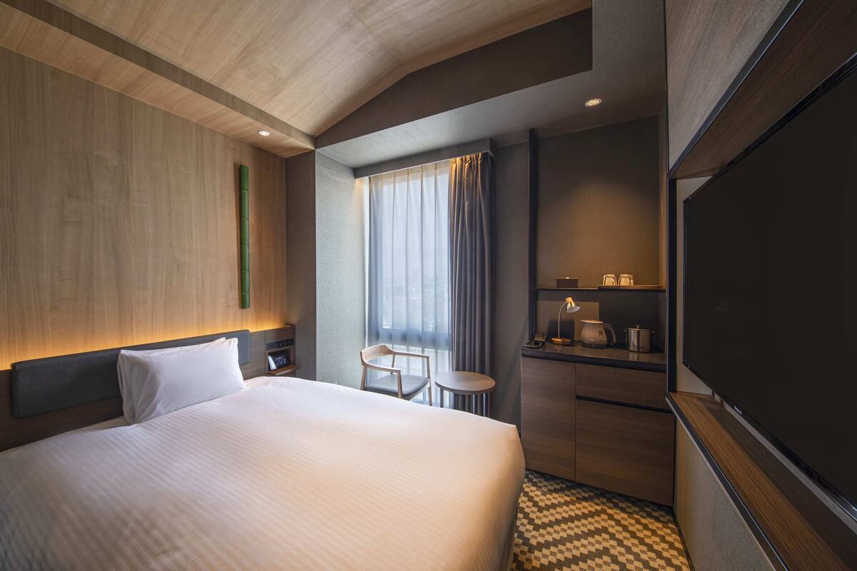 Een hotelkamer met een groot bed, een bureau met stoel, een tafeltje, een raam met gordijnen en een flatscreen televisie.
