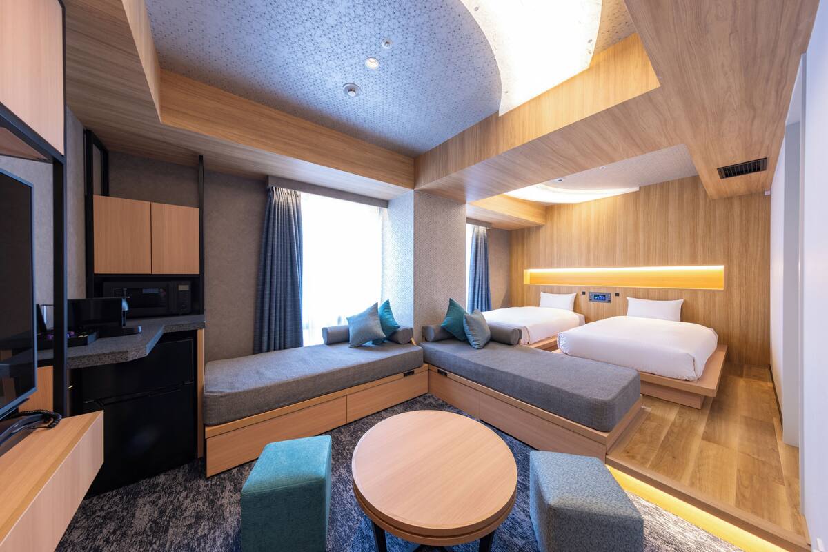Een moderne hotelkamer met een slaapbank, een klein rond tafeltje, een televisie en een bureau met een computer.