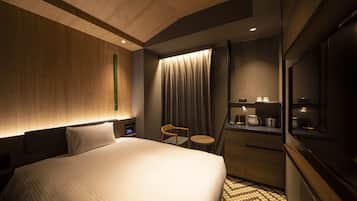 A hotel room with a large bed, a desk with a chair, a small table, a TV, and a minibar.