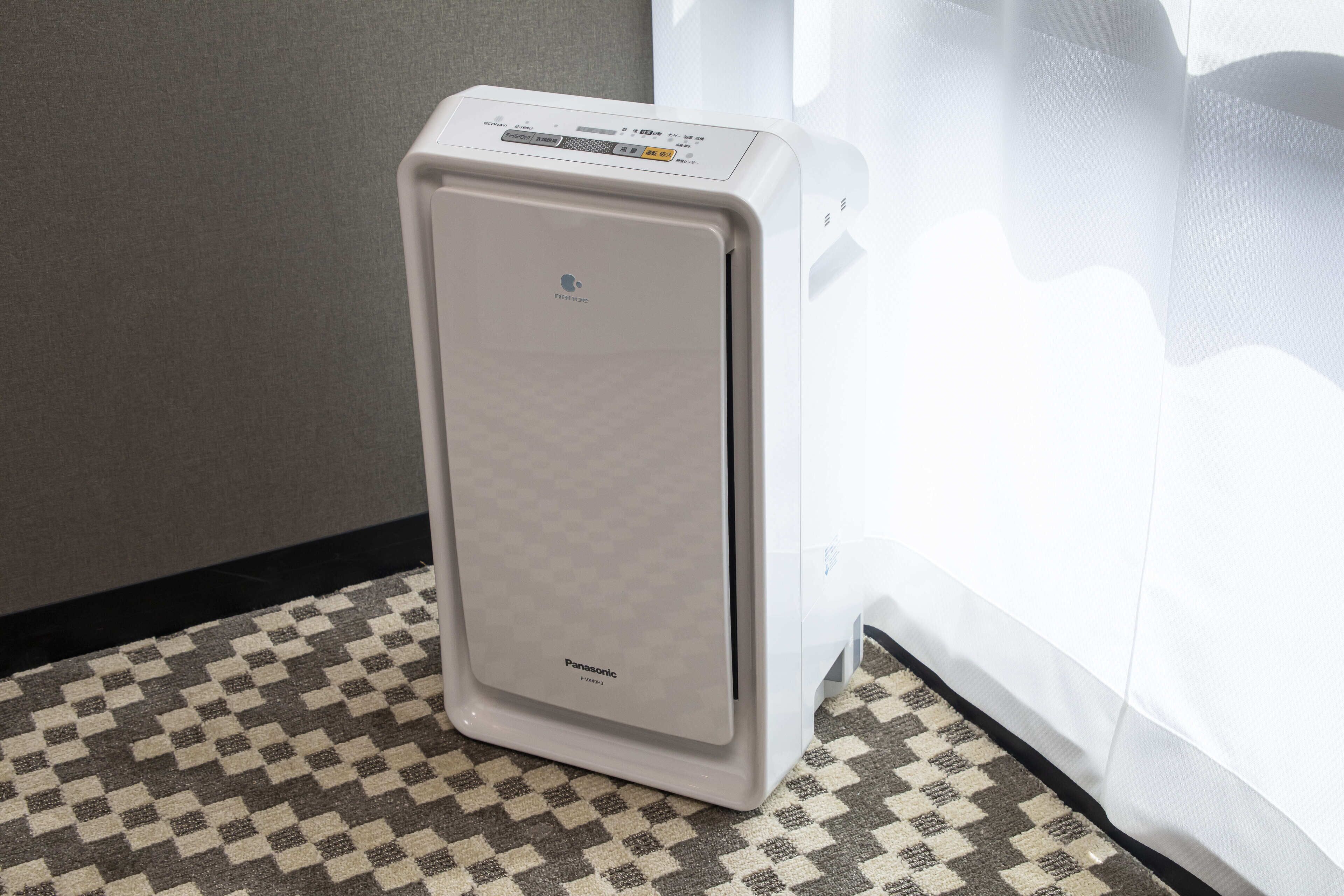 A white Panasonic portable air conditioner in a corner with a patterned floor.