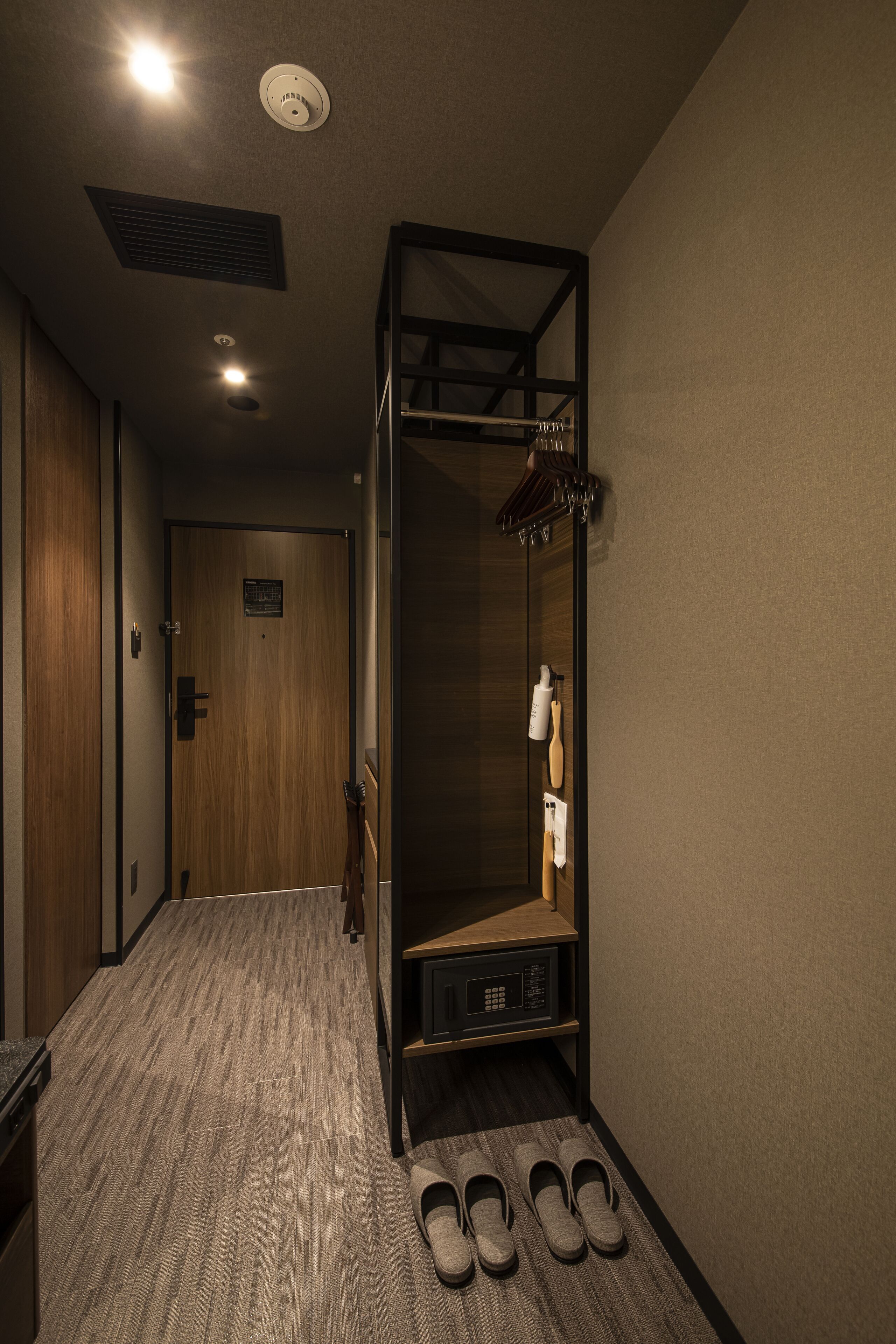 Ein Hotelzimmer mit Holztür, einer eingebauten Sitzbank mit Kleiderhaken und einem Paar Hausschuhen auf dem Boden.