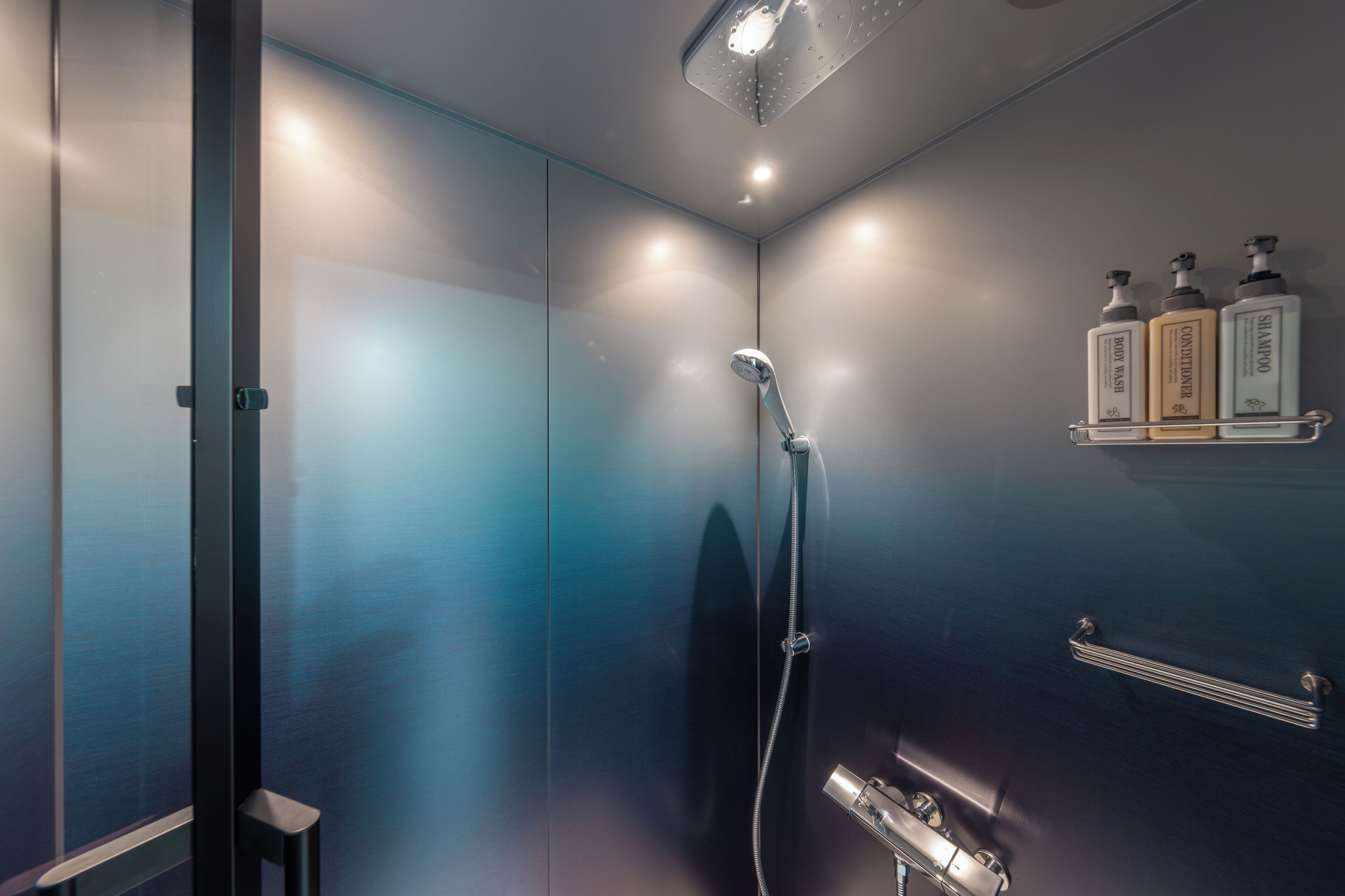 A modern bathroom with a shower, a towel rack, and three bottles of toiletries on a shelf.