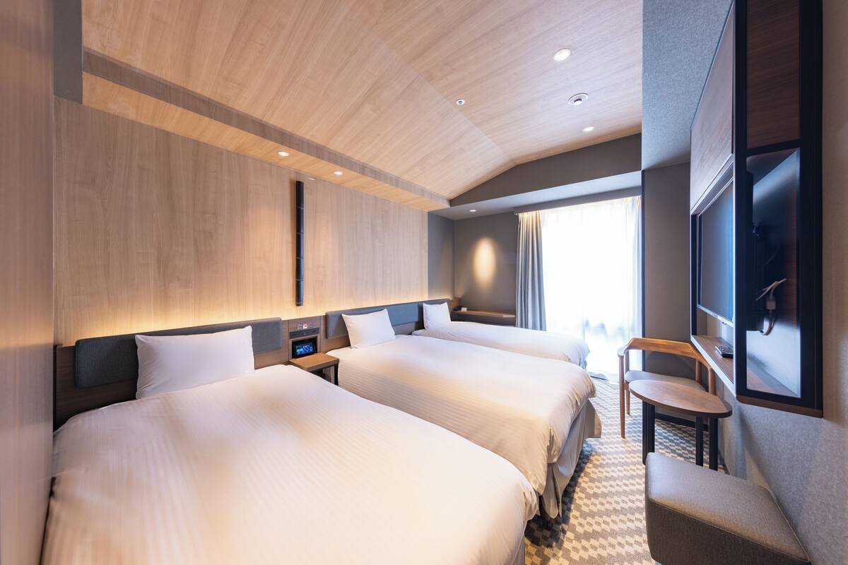 Een hotelkamer met twee bedden, een bureau, een stoel, een televisie en een raam met gordijnen.