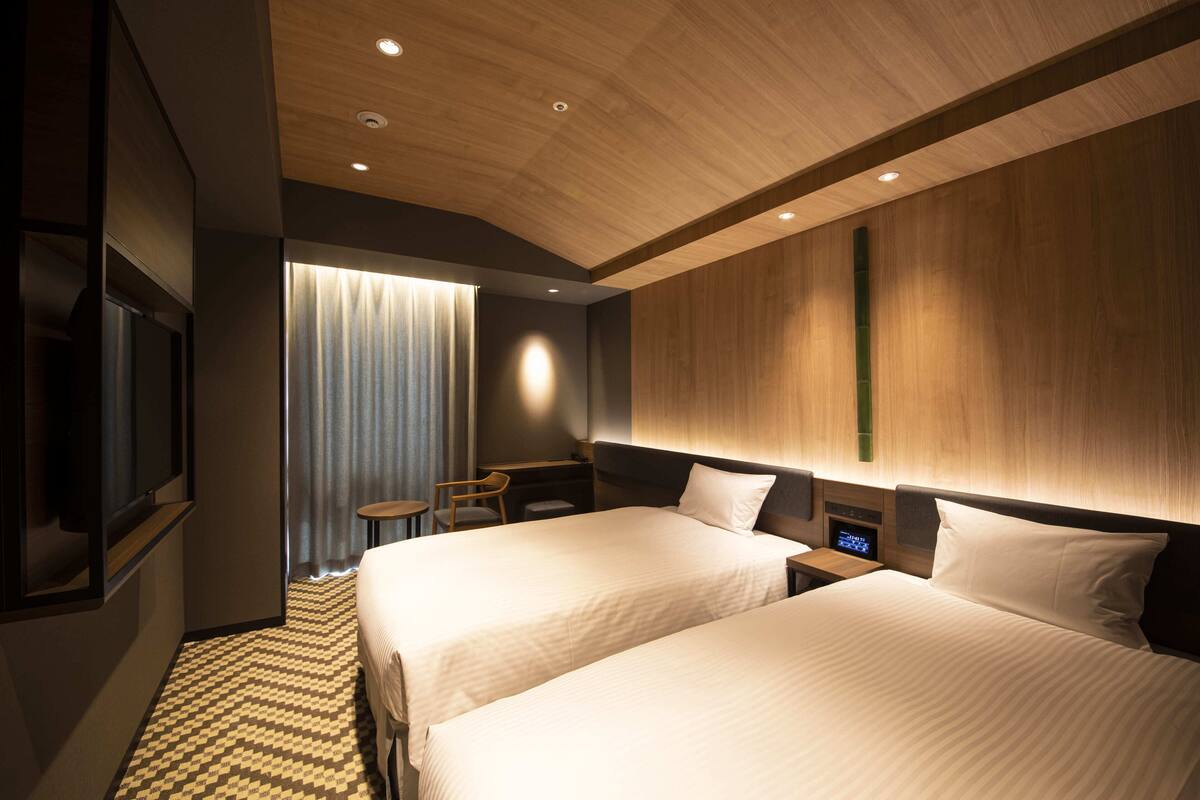 Een hotelkamer met twee bedden, een bureau, een stoel, een televisie en een bedieningspaneel.