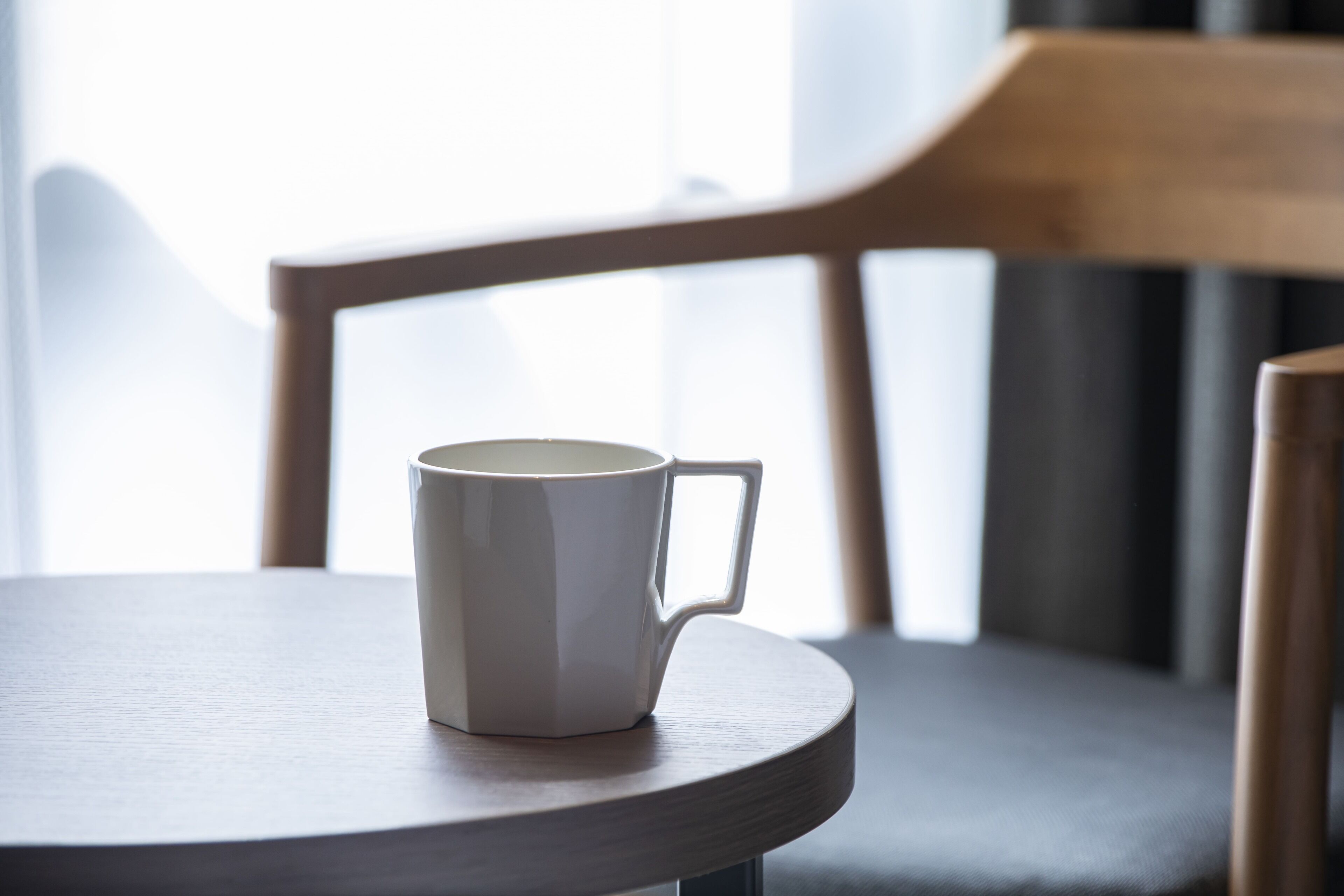 Una taza blanca sobre una mesa de madera redonda, con una silla al fondo.