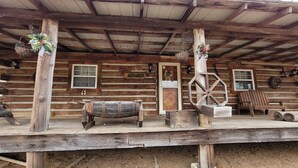 A rustic wooden cabin with a porch, a wheelbarrow, and a bench.