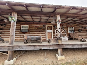 A rustic wooden cabin with a porch, a wheelbarrow, and a bench.
