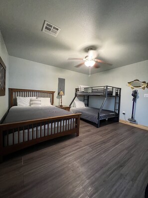 A room with a wooden bed, a bunk bed, a ceiling fan, and a wall-mounted air vent.