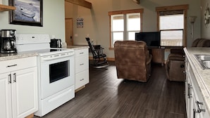 A kitchen with white appliances, a dining area with a brown leather chair, and a TV. - Waterfront!! Private Pier! Reel Relaxing, Real Fun On Sabine Lake (Port Arthur)