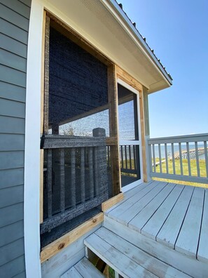 Une terrasse en bois avec une rambarde, une fenêtre munie d’un moustiquaire et une vue sur une jetée et l’eau.