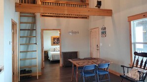 A loft-style room with a wooden staircase, a dining area with blue chairs, and a bed in the background. - Waterfront!! Private Pier! Reel Relaxing, Real Fun On Sabine Lake (Port Arthur)