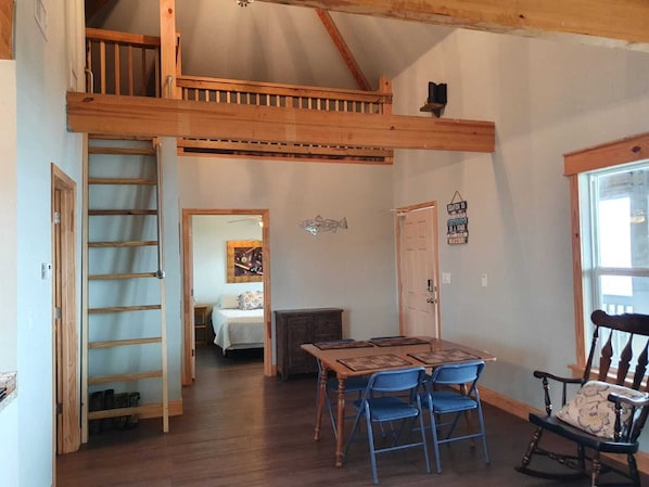 A loft-style room with a wooden staircase, a dining area with blue chairs, and a bed in the background. - Waterfront!! Private Pier! Reel Relaxing, Real Fun On Sabine Lake (Port Arthur)