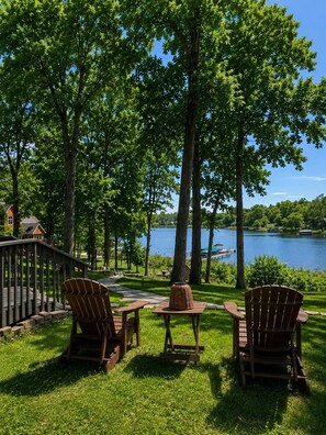A lakeside deck with Adirondack chairs, a picnic table, and a view of a lake.