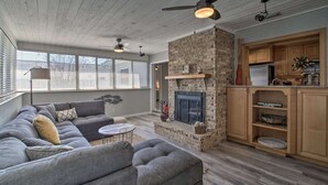 A living room with a stone fireplace, a gray sofa, and a kitchen area with wooden cabinets.